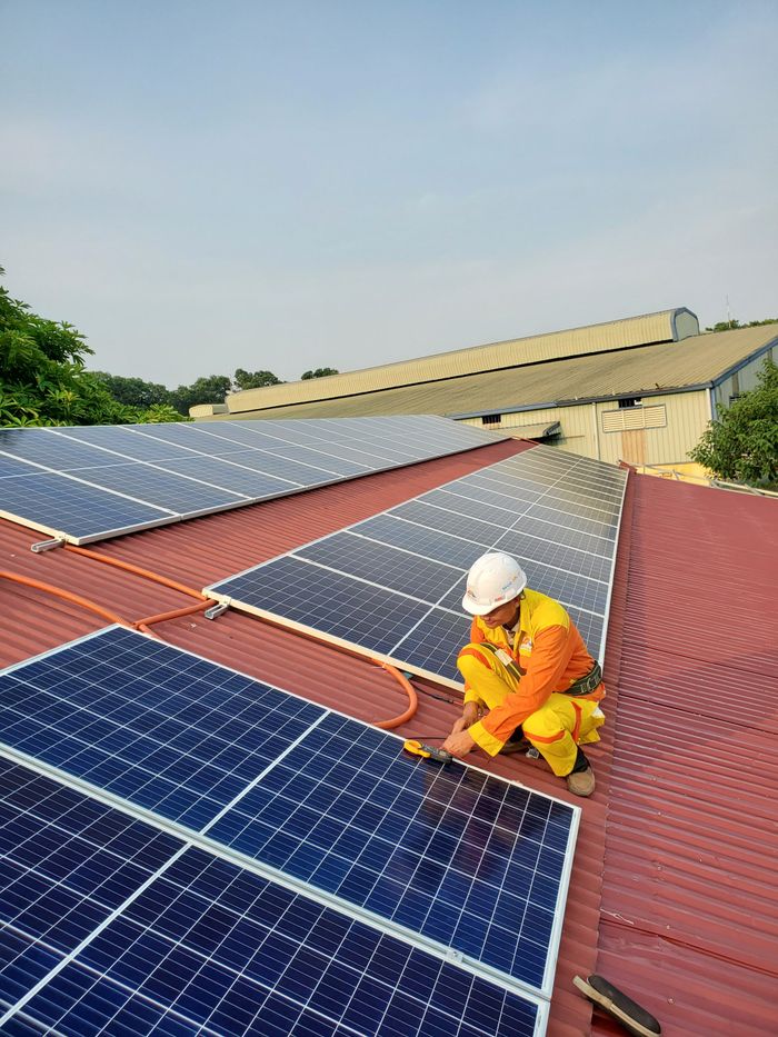 services-04 Technician working on solar panel installation on a rooftop under clear sky.