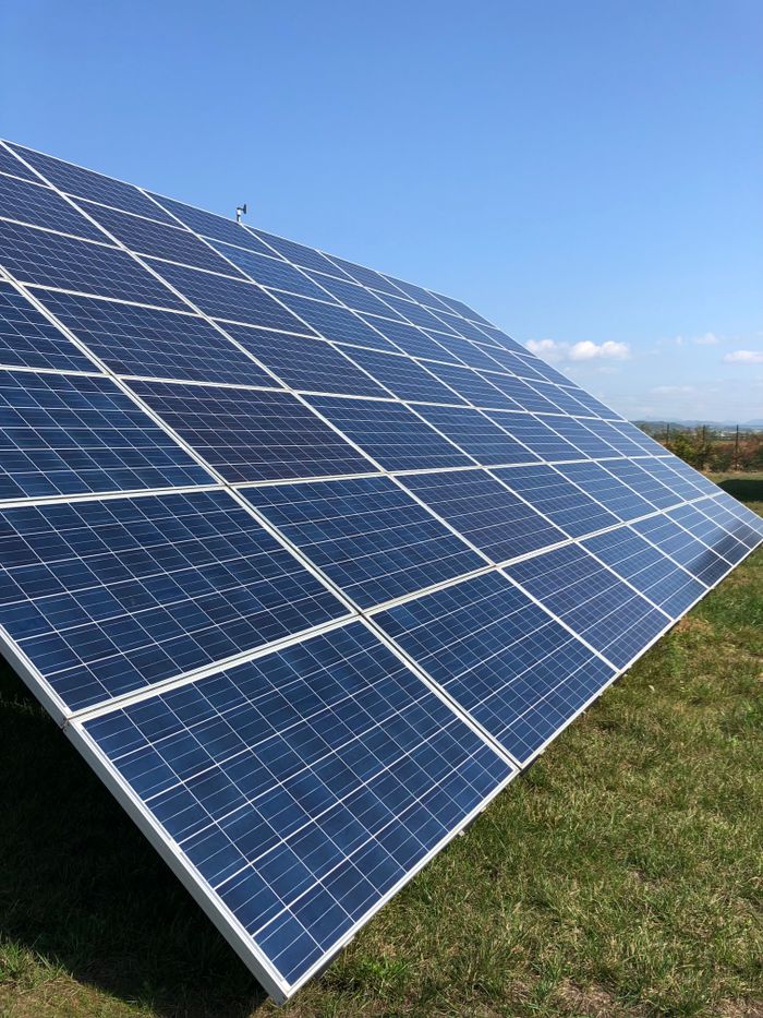 about-us-02 Solar panels in a green field on a sunny day, showcasing renewable energy in Tortona, Italy.