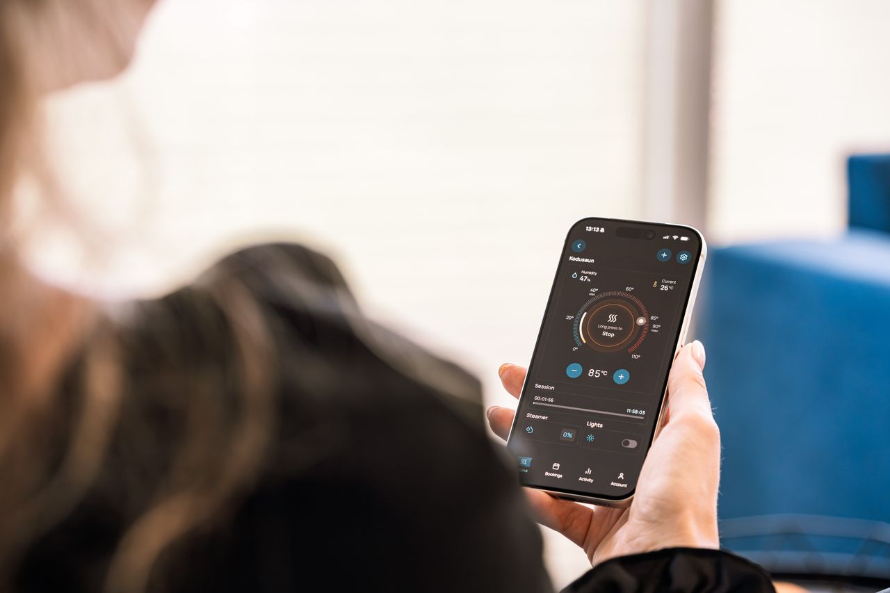 about-us-02 A woman holding a smartphone displaying a sauna control app, highlighting modern sauna technology.